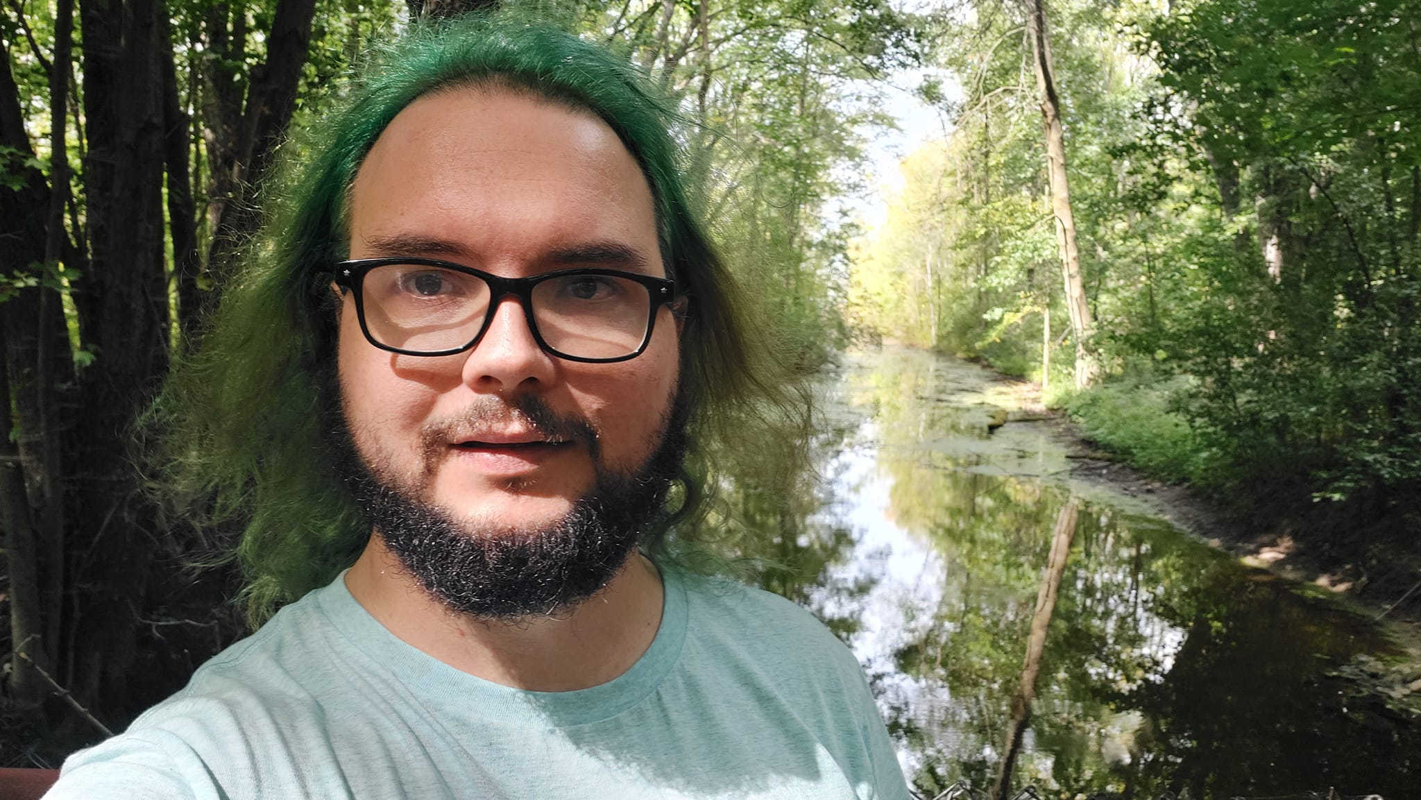 A man with green hair stands on a dam with a channel extending behind him, Photo 2